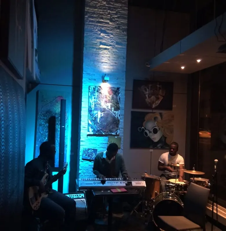A jazz trio — guitar, keys and drums — performing live at Kawa Espresso Bar under blue stage light