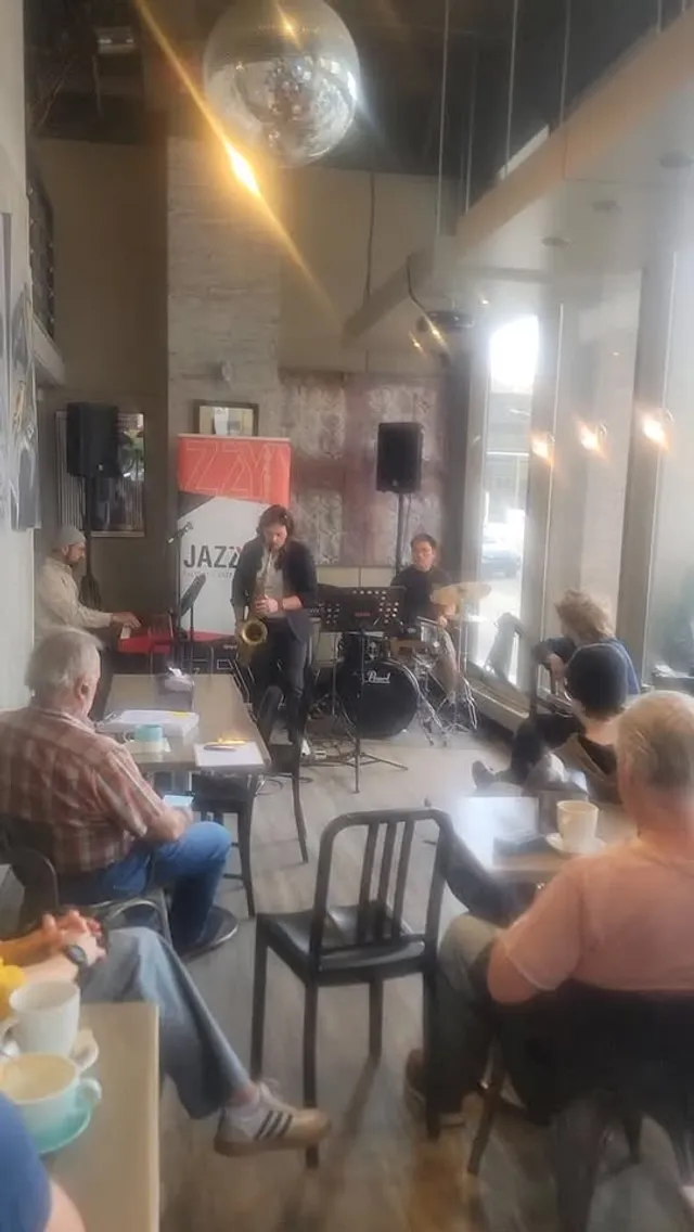 A saxophonist playing a live afternoon jazz set at Kawa Espresso Bar, with guests at tables and coffee cups